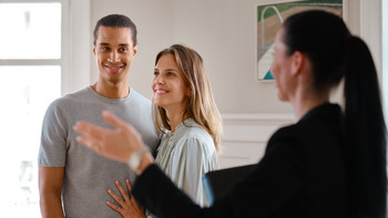 Eine Maklerin zeigt einem jungen Pärchen an einer Besichtigung eine Wohnung