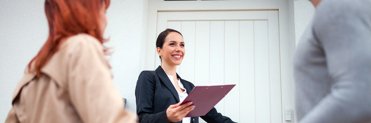 Immobilienmaklerin vor Immobilie mit Paar