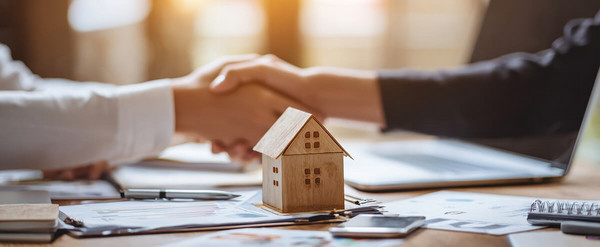 Modellhaus und Dokumente auf Tisch und Handschlag 