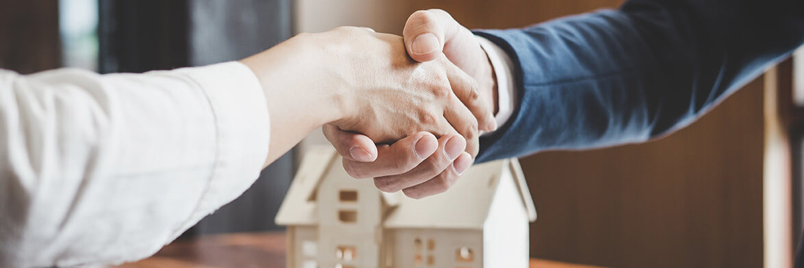Personen geben sich einen Handschlag mit Modellhaus im Hintergrund
