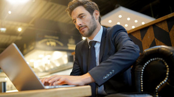 Makler sitzt in einem Kaffeegeschäft an seinem Laptop und arbeitet