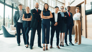 Eine Gruppe von Menschen in Business-Kleidung steht nebeneinander und schauen in die Kamera