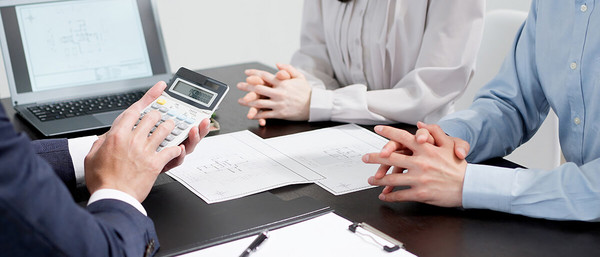 Personen sitzen an Tisch mit Taschenrechner und Dokumenten