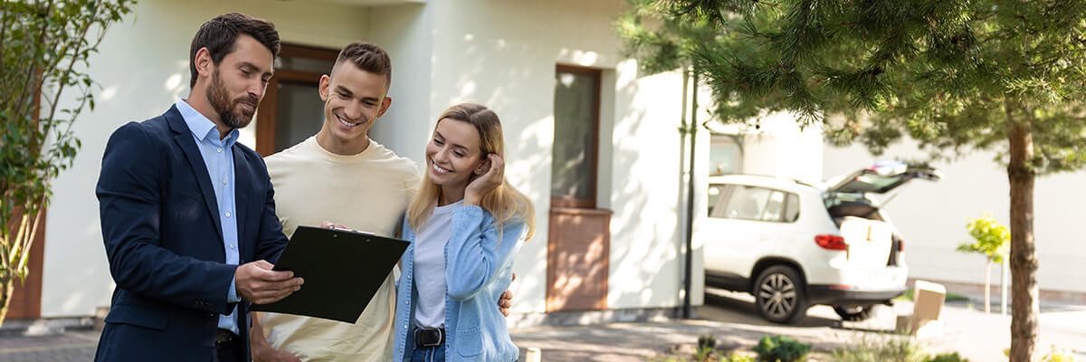 Immobilienmakler zeigt lächelndem Paar Dokument vor Haus