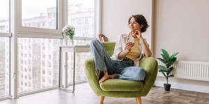 Eine Frau mit dem Smartphone in der Hand sitzt auf einem grünen Sessel