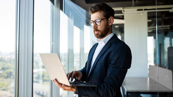 Makler steht mit Laptop in der Hand